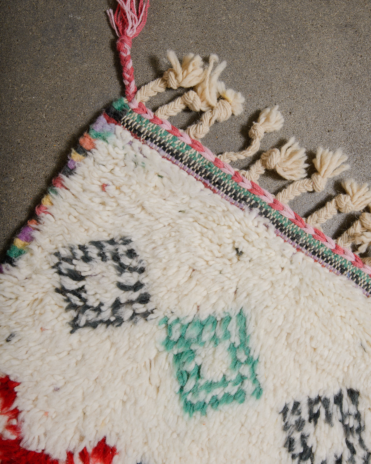 Corner of wool berber rug that is finished with tightly woven colourful wool and natural wool tassels across the ends.